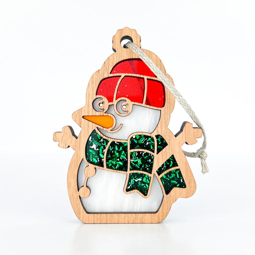 The Forged Flare® Christmas Snowman Ornament, 3.6", is perfect for your holiday decor. It wears a red hat and a green scarf. With an orange carrot nose and a braided linen string for hanging, this charming decoration adds festive cheer to any space.