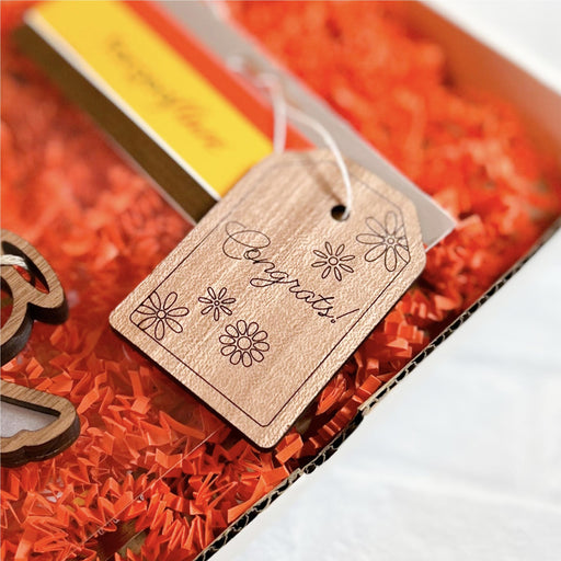 Close-up of a handcrafted gift tag reading "Congrats!" attached to a Mother’s Angels® ornament.