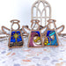 Three 3.5" angel figurines from the Forged Flare® Mother's Angels® Christmas Nativity 3-Piece Bundle - Star, Mary and Joseph are displayed on a terrazzo surface. Each ornament features nativity scenes of Mary and Joseph holding baby Jesus, along with a star. A decorative arch-shaped window is in the background. These Christmas nativity ornaments make perfect angels for tree decoration.