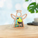 A Mother's Angels® Goldfinch Ornament from Forged Flare®, this 3.5" decorative wooden angel figurine features cut-out wings and a colorful illustration of a goldfinch perched on branches at its center. The softly blurred background highlights a plant and stones, making it an ideal heartfelt memorial gift or addition to any bird lover's collection.