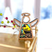 The Goldfinch Ornament from Forged Flare's® Mother's Angels® collection is a 3.5" wooden angel figurine featuring a hole for a halo, transparent wings, and a body depicting a yellow and black bird amid greenery. Perfect as a gift for bird lovers, it's hanging from a string on a gold-colored surface with blurry festive decorations in the background.