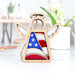 The American Flag Ornament by Forged Flare® is a 3.5" angel figurine from the Mother's Angels® series, boasting stained glass–style wings and a U.S. flag body with stars and stripes. It makes an ideal patriotic gift or Christmas tree ornament. Displayed on a white surface, the background features blurred plants and home decor items.