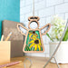 A wooden ornament featuring the intricate details of a Black-Eyed Susan flower, complete with yellow petals and green leaves, hangs from a string against a backdrop of a white tiled wall, alongside a plant and a desk area filled with stationery items. The Black-Eyed Susan Ornament angel figurine from Mother's Angels® by Forged Flare® makes for an exquisite flower gift.