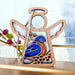 Introducing the Bluebird Ornament by Forged Flare®, a 3.5" wooden angel figurine from the Mother's Angels® collection. This charming piece features transparent wings and a halo, with a blue and brown bird perched on holly adorned with red berries. It hangs elegantly from a silver string, set against a backdrop of a blurred window and holiday decorations—making it the perfect gift for any bird lover.