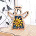 The Celestial Sun Ornament from Forged Flare® is a 3.5" Mother's Angels® figurine that hangs by a string, featuring a wooden angel with white wings and a halo. The angel's body displays a colorful sun with yellow and orange rays against a blue glittery background. It is set on a wooden surface, accompanied by a bird decoration in the background.