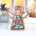 A stunning Columbine Ornament | 3.5" Angel Figurine | Mother's Angels® from Forged Flare® with a stained glass–style body featuring a floral design hangs in front of a sunlit window. Behind this beautiful Christmas ornament, blurred indoor plants and decorative objects create a cozy and bright background.