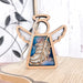 A Feather Ornament from the Mother's Angels® collection by Forged Flare®, featuring a 3.5" wooden angel figurine with carved wings and a hollow circular head, rests on a light-colored wooden surface. The angel showcases an intricate feather design with blue and white accents on the body and includes a string for hanging, making it an ideal Christmas tree ornament. In the blurred background, a bird silhouette can be seen.