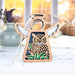 The Forged Flare® Owl Ornament | 3.5" Angel Figurine from the Mother's Angels® collection is displayed on a white surface. The background showcases blurred autumn decorations, including pumpkins and a vase, all illuminated by warm, soft lighting from a window. This charming owl ornament features intricate cutout details and includes a string for hanging, making it the perfect gift for bird lovers.