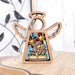 On a wooden surface stands the Red, White & Bloom Ornament—a 3.5" angel figurine from Mother's Angels®, offered by Forged Flare®. This decorative wooden ornament features a halo and wings with an open center showcasing vibrant flower-themed stained glass details. In the background, a blurry metal wall art piece depicting birds on branches is visible, making it an ideal heartfelt Patriotic Gift for any occasion.