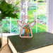 A Seahorse Ornament | 3.5" Angel Figurine from Mother's Angels® by Forged Flare® stands gracefully on a closed hardcover book on a table by a window overlooking a lush garden. A vase with white flowers is partially visible in the background, creating an enchanting scene.