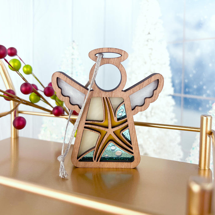 A Forged Flare® Starfish Ornament | 3.5" Angel Figurine from the Mother's Angels® collection stands on a golden shelf. In the background, festive decorations and a snowy window scene, with branches bearing red berries, add a touch of color. Consider this unique gift idea for women, perfect for the holiday season.