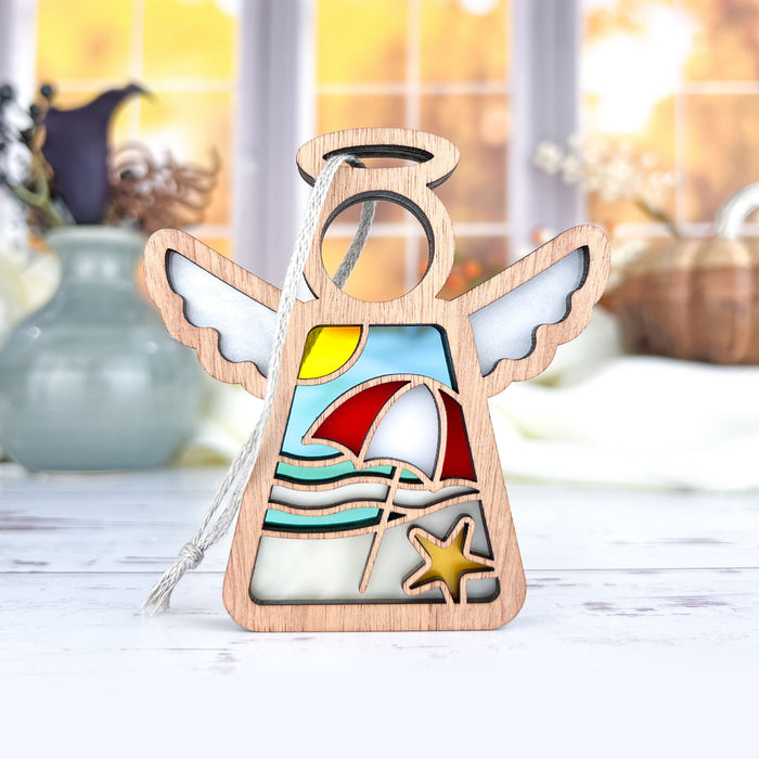 A Summer Beach Ornament from Forged Flare®, featuring a 3.5" angel figurine, is displayed on a white surface. The wooden piece showcases a beach scene with an umbrella, ocean waves, and a starfish. In the background, vases and a window revealing an autumn landscape are visible. Perfect as a last-minute Mother's Day gift or as a Christmas tree ornament.