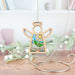 The Book Lovers Ornament by Forged Flare®, a 3.5" angel figurine from Mother's Angels®, elegantly hangs on a spiral stand and makes an ideal gift for authors. Adorned with stained glass accents, its body showcases a charming daisy and leaves design. Set against a wooden surface with softly-focused white branches and decor, this piece creates an enchanting atmosphere for any writing space.