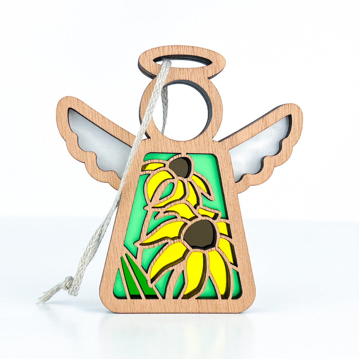 The Black-Eyed Susan Ornament by Forged Flare®, part of the Mother's Angels® collection, showcases a 3.5" wooden angel figurine with a circular head, outstretched wings, and a halo. The angel wears a green dress adorned with yellow sunflowers featuring brown centers and hangs gracefully by a white string.