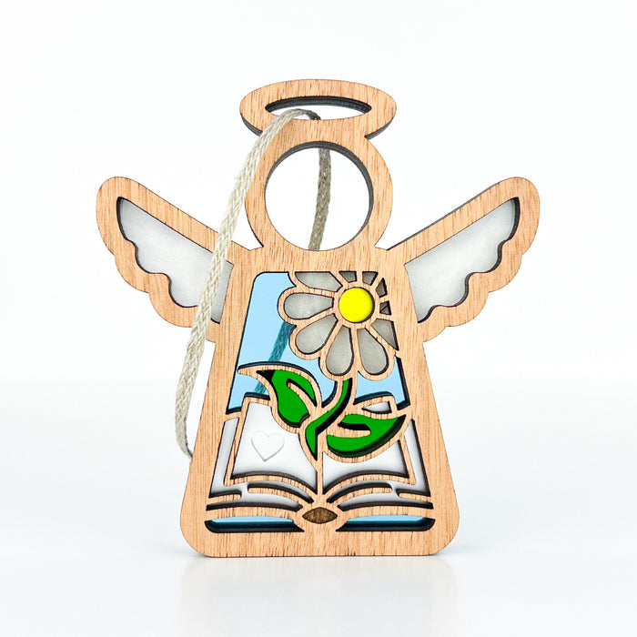 The Book Lovers Ornament by Forged Flare®, part of the Mother's Angels® collection, is a 3.5" wooden angel figurine with open wings and a halo. Featuring a daisy and leaves design with an open book at the base, this ornament has white accents on the wings, a blue background, and a braided linen string at the top for hanging—perfect as both a Christmas tree ornament and a book club gift.