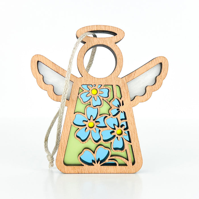 Introducing the Forget-Me-Not Ornament by Forged Flare®, a 3.5" angel figurine from the Mother's Angels® collection. This charming wooden angel ornament features a cutout design with delicate blue forget-me-not flowers against a green background. The angel is depicted with outstretched wings and a circular halo, and it includes a string for easy hanging. The flowers have yellow centers, adding an extra touch of charm to this handmade-looking décor piece.