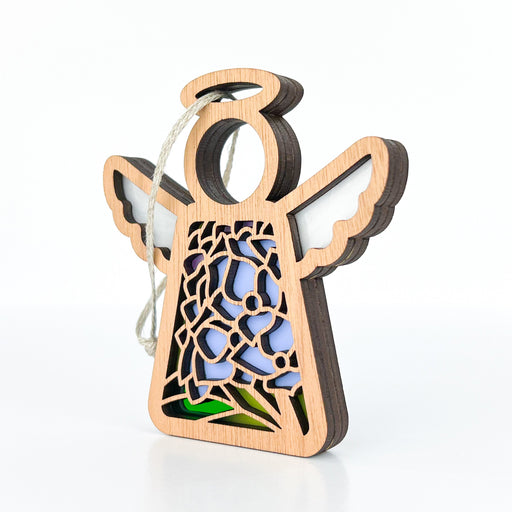 The Hydrangea Ornament by Forged Flare®, part of the Mother's Angels® collection, is a 3.5" wooden angel figurine featuring cutout detailing that reveals a blue and green stained glass-like design inside. This piece showcases outstretched wings and a halo, with a string at the top for hanging on your Christmas tree. The background is plain white.