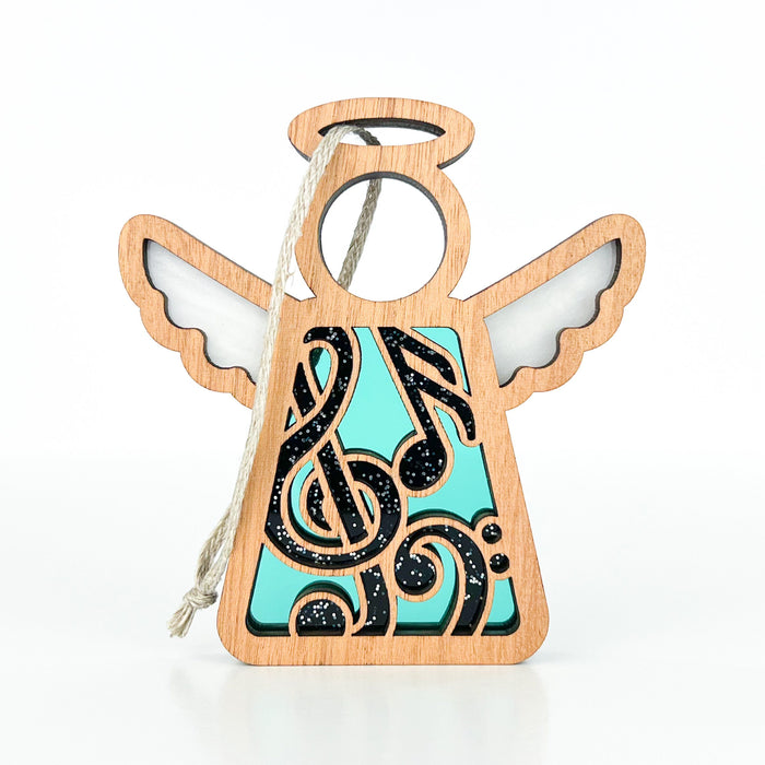 The Music Ornament from Forged Flare’s Mother's Angels® collection makes a perfect gift for any music teacher. This 3.5" wooden angel figurine features a turquoise body decorated with black musical notes and symbols, complete with outstretched wings, a halo, and an attached string for hanging. The upper wings and halo are intricately cut out to reveal a lighter background.