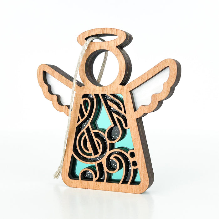 A 3.5" Music Ornament Angel Figurine from Forged Flare®’s Mother's Angels® collection stands against a white background. This exquisite music teacher gift features a wooden angel with a halo, wings, and intricate cut-out details. Musical notes are meticulously carved into its body and it is painted in shades of turquoise and black. It also includes a hanging braided linen string.