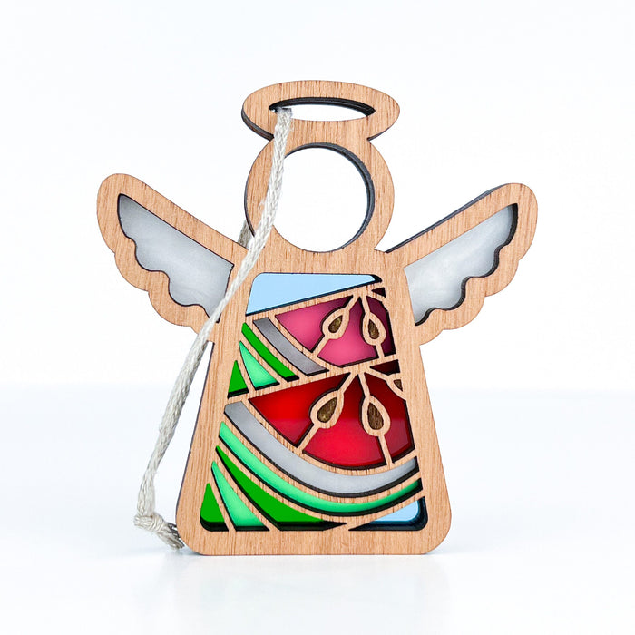 This Summer Watermelon Ornament by Forged Flare® is a small, wooden angel figurine from the Mother's Angels® collection. It features white wings, a round halo, and colorful stained glass-style panels in red, green, and blue on its body. A white string is attached to the top for easy hanging against a white background. Perfect as a 3.5" Christmas tree ornament.