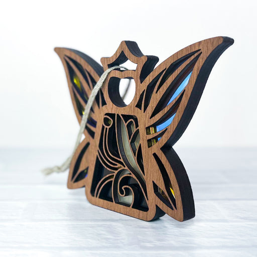 The Fairy - Legacy Edition Honeysuckle Ornament by Forged Flare® is a 3.7" butterfly-shaped wooden ornament with intricate patterns. It features a string for hanging and is displayed on a light-colored surface, making it an ideal housewarming gift.
