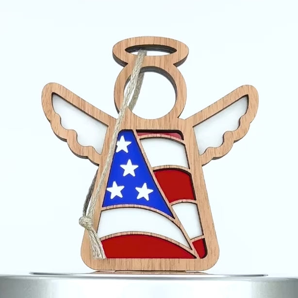 Wooden angel ornament with an American flag design, featuring red, white, and blue colors with stars and stripes, hanging on a white background.