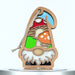 A decorative wooden gnome ornament in the shape of a gnome, featuring a colorful stained glass–style design with a red hat, a yellow toadstool mushroom, and a green patch. The gnome has a white beard and hangs by a braided linen string through a hole in the tip of the hat.